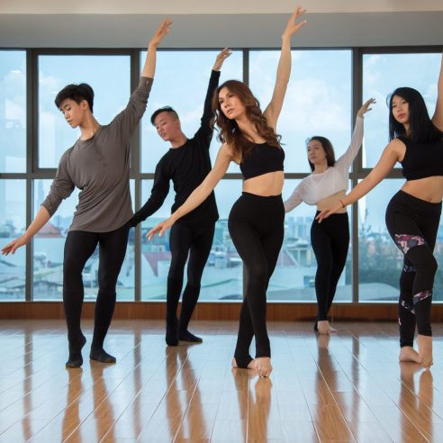 Group of attractive Asian people performing graceful dance movement while dancing in stylish studio together