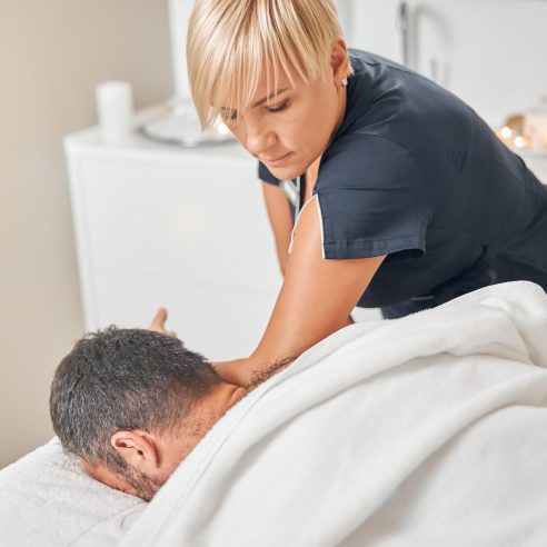 Young man receiving therapeutic back massage while lying on massage table